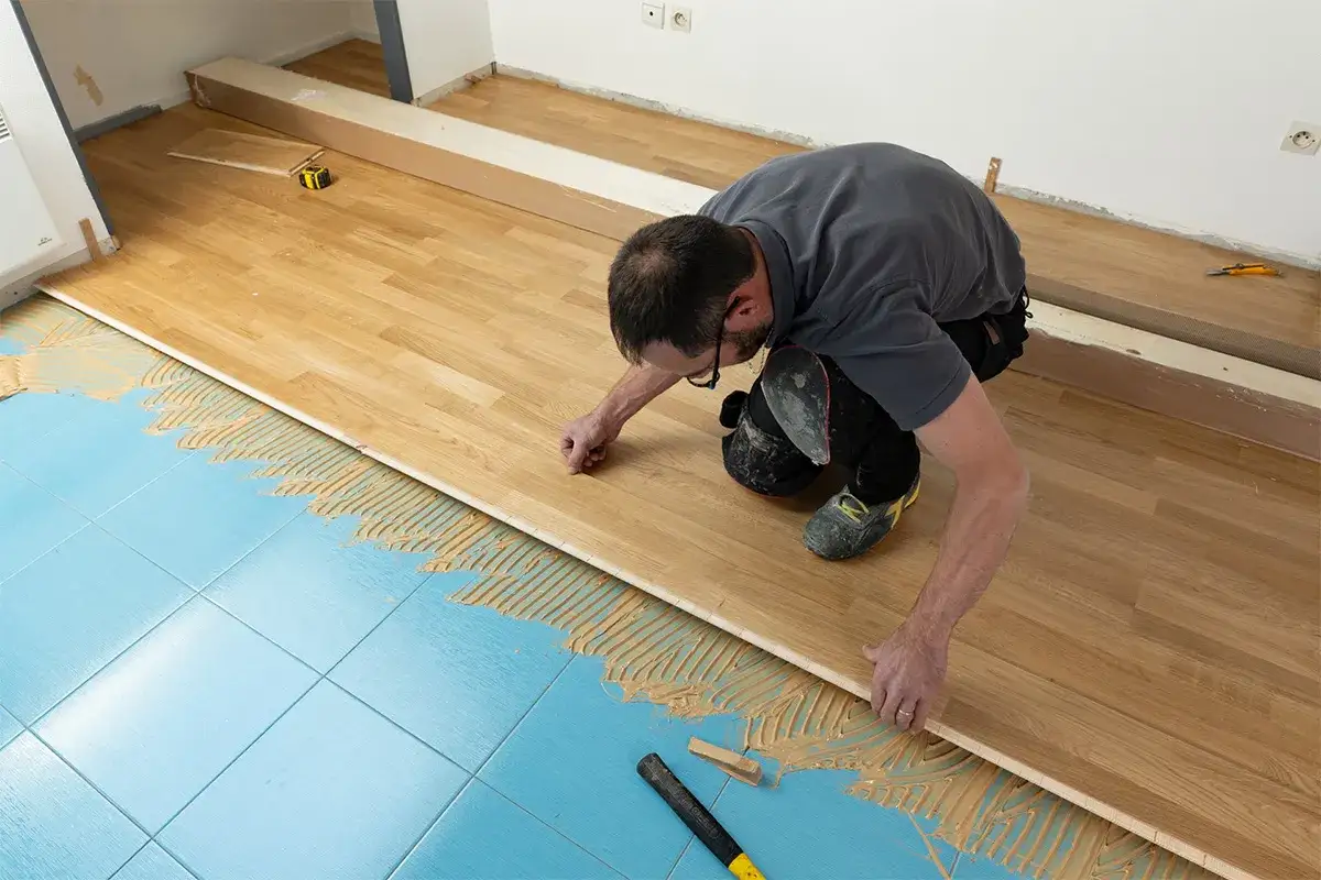 Pose d'une sous couche parquet sur carrelage. Un homme pose des lames de parquet sur une sous-couche bleue, avec de la colle appliquée sur le carrelage.
