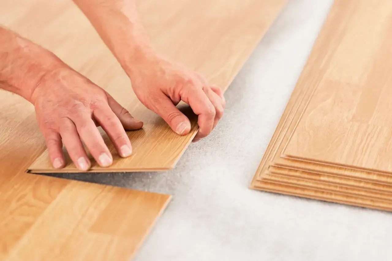 Mains assemblant des lames de parquet flottant. L'épaisseur du parquet flottant est visible lors de l'installation.