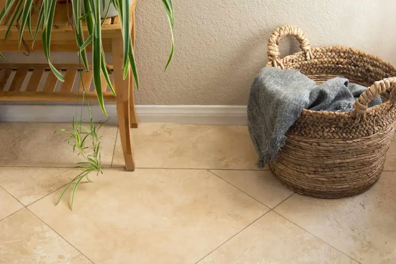 Un coin cosy avec un mélange travertin et carreaux de ciment, une plante retombante et un panier en osier rempli d'une couverture grise.
