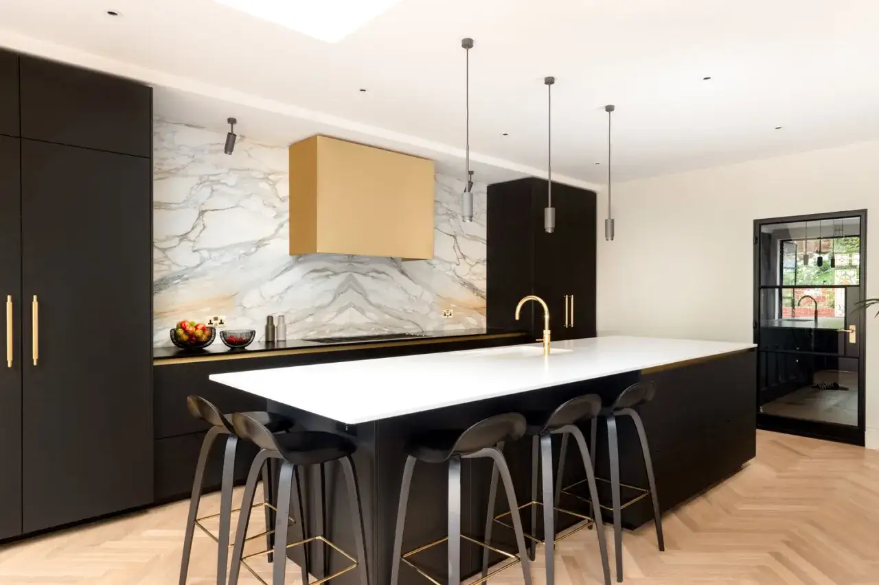 Cuisine moderne aux finitions noires et dorées, avec un îlot central et un mur en marbre spectaculaire. Une vision de cuisine architecte d'intérieur.