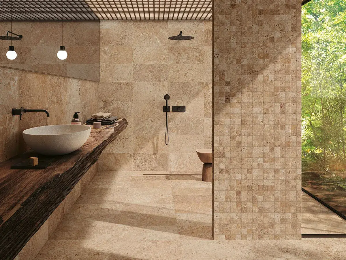 Une salle de bain moderne avec un lavabo en pierre, un plan de travail en bois brut et une douche à l'italienne. Le carrelage en travertin crée une ambiance chaleureuse et naturelle.