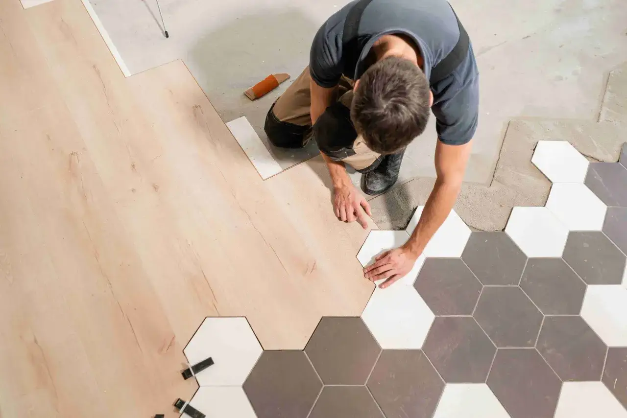 Un ouvrier pose du carrelage hexagonal sur un sol en bois.