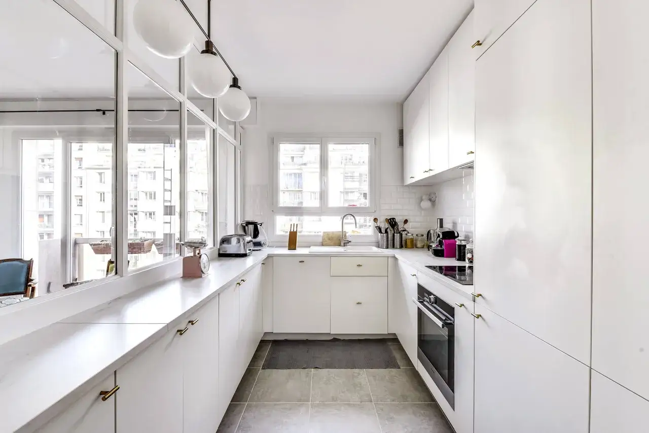 Cuisine salle &agrave; manger en longueur, blanche et lumineuse, avec plan de travail en marbre, &eacute;vier, four et rangements.