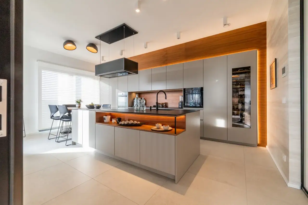 Plan cuisine en L moderne avec &icirc;lot central, armoires grises, bois chaleureux et &eacute;clairage d'ambiance.