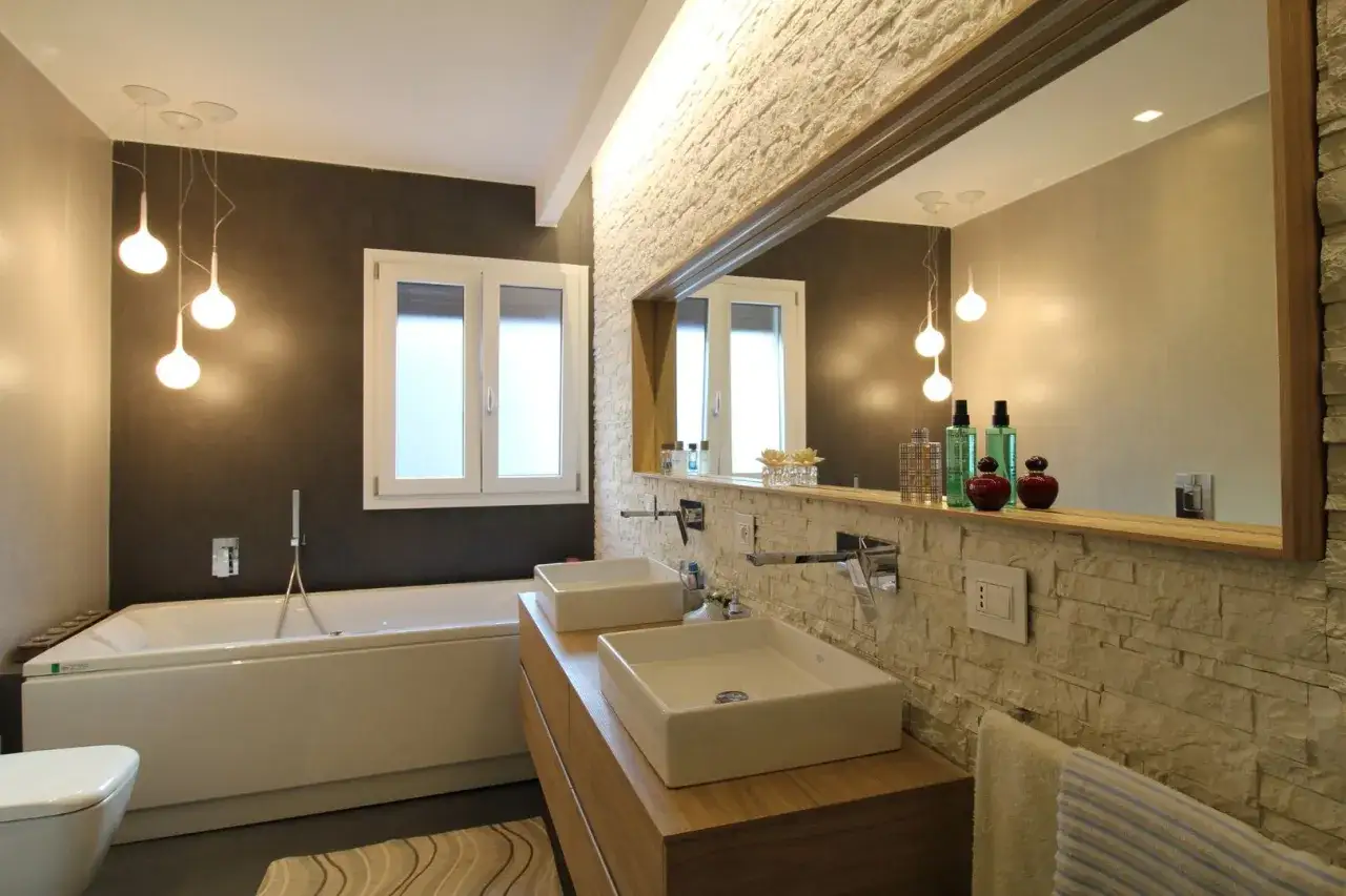 Salle de bain moderne avec baignoire, double vasque et mur en pierre. Une belle idée rénovation salle de bain pour un espace élégant.