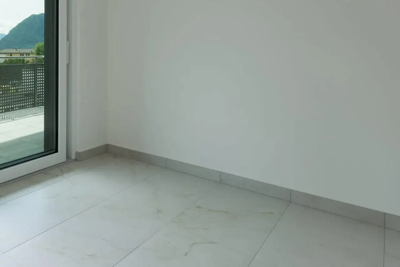 Coin d'une pièce avec sol carrelé marbré et plinthe discrète. La hauteur de la plinthe carrelage est subtile, soulignant la finition soignée.