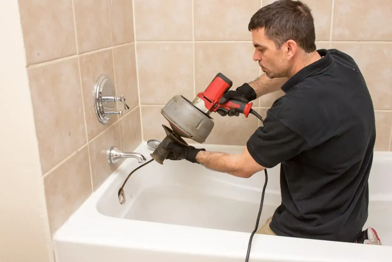 Un plombier utilise un furet pour d&eacute;boucher une canalisation dans une baignoire.