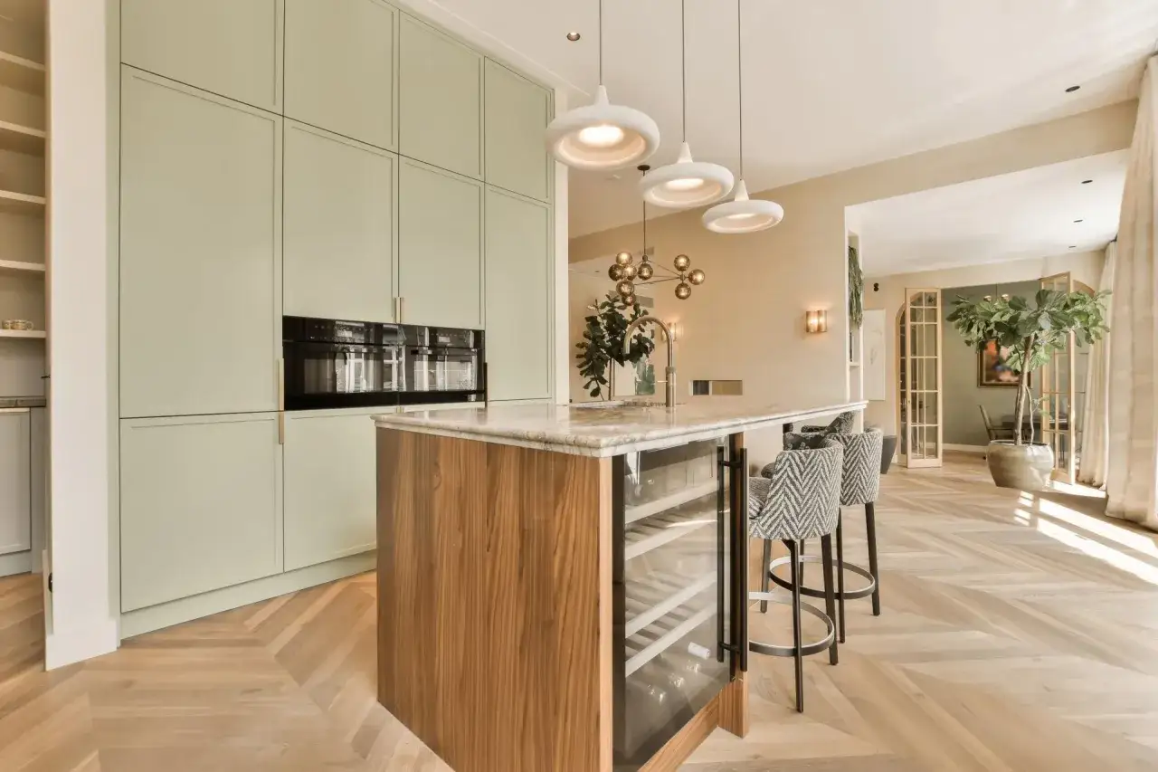 Cuisine moderne avec îlot central, armoires vert pâle et un magnifique parquet au sol en chevrons.