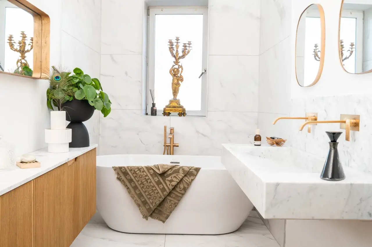 Salle de bain petite et élégante avec baignoire îlot, lavabo en marbre, robinetterie dorée et décoration raffinée.