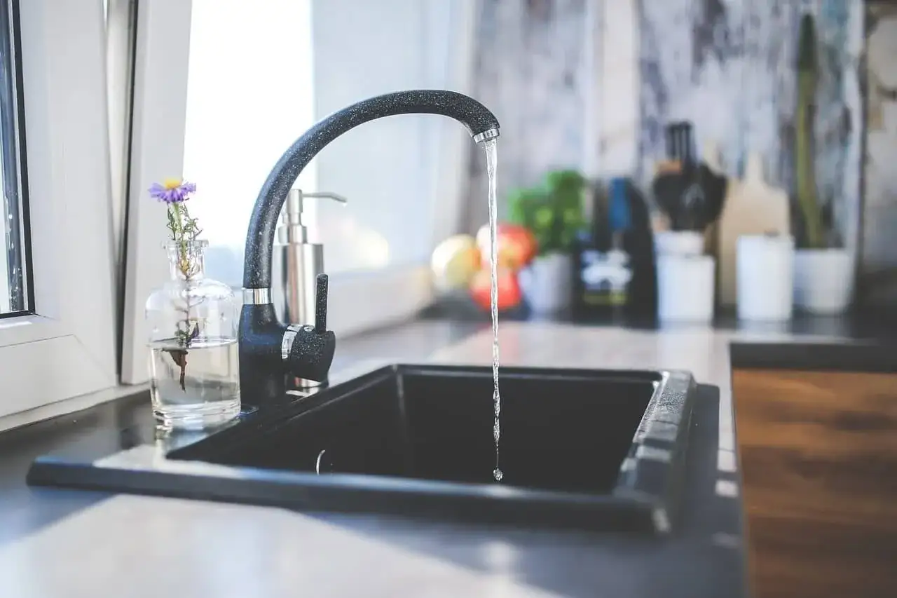 Un robinet noir verse de l'eau dans un &eacute;vier, symbolisant la filtration eau du robinet pour une cuisine moderne et saine.