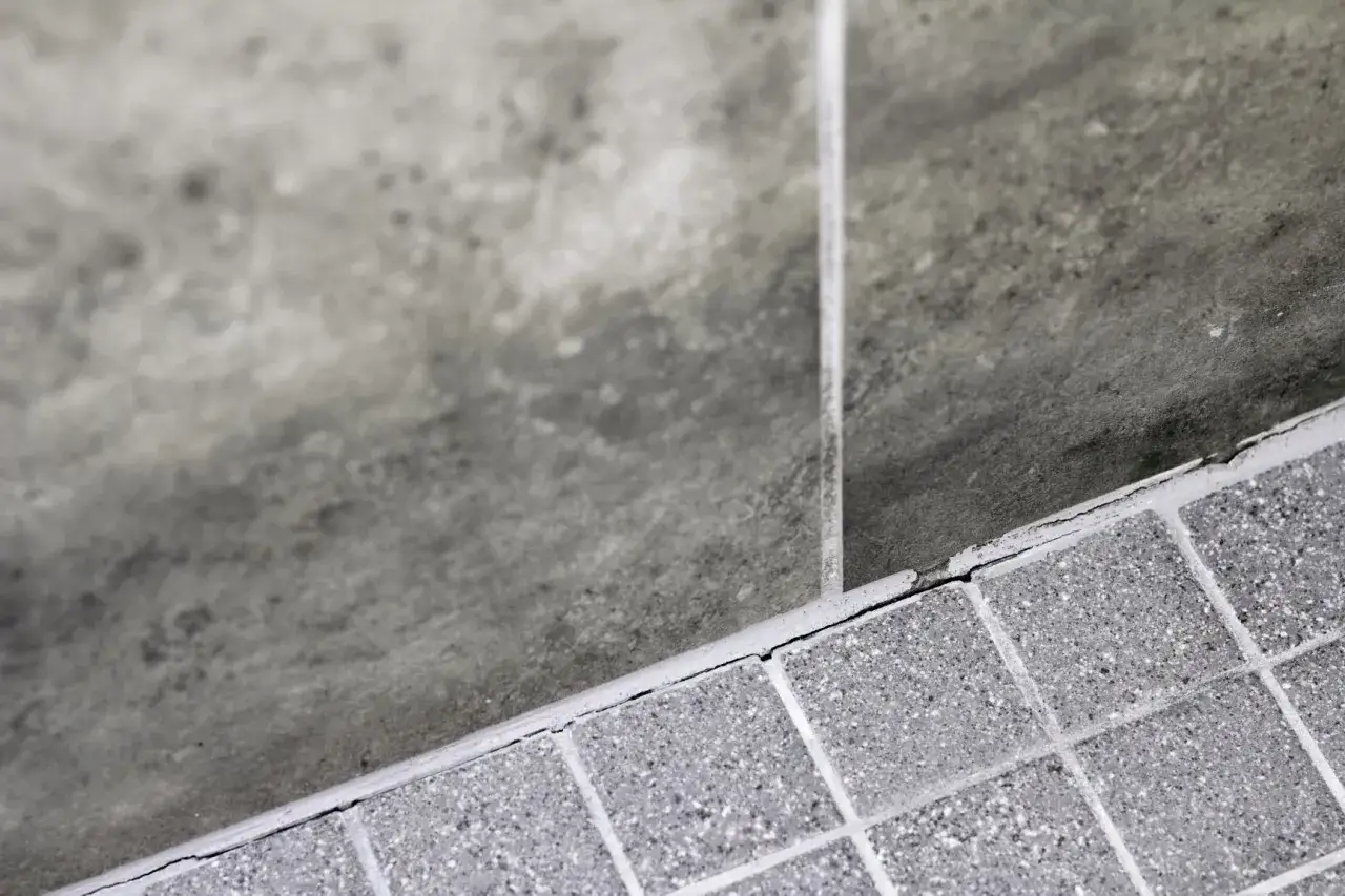 Gros plan sur un carrelage mal posé, avec des fissures visibles le long du joint. La texture granuleuse des carreaux contraste avec la surface plus lisse et sombre adjacente.