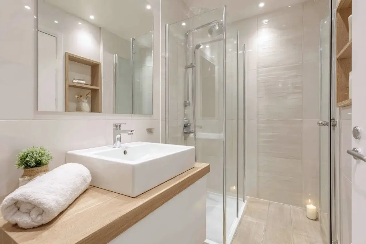 Une petite salle de bain moderne avec une douche vitrée, un lavabo rectangulaire sur un meuble en bois clair, et une serviette blanche pliée.