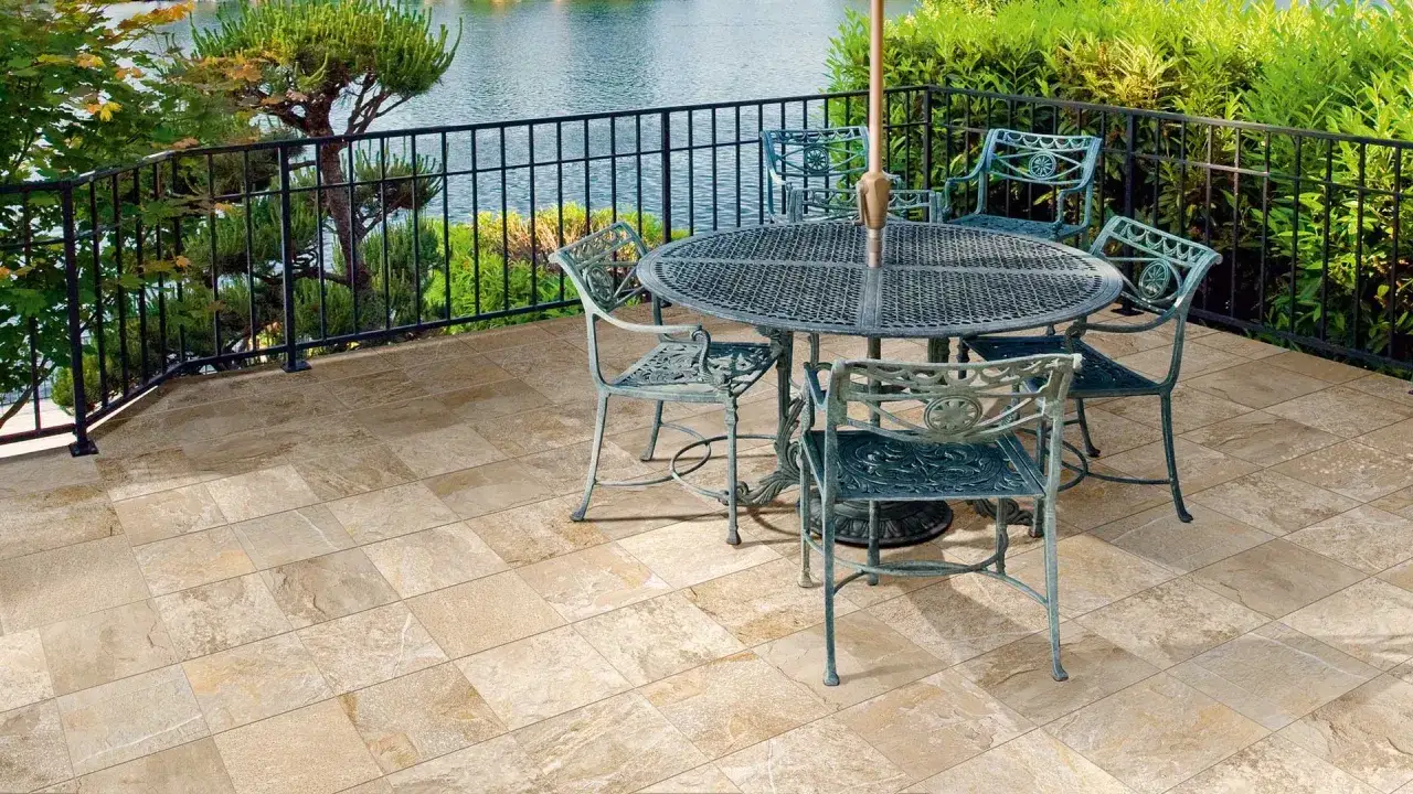 Terrasse avec mobilier de jardin sur un sol en grès cérame émaillé aux tons sable, surplombant un plan d'eau entouré de verdure.