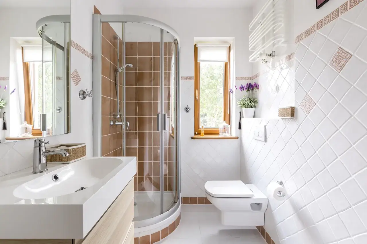 Salle de bain moderne avec lavabo, miroir, et une cabine de douche aux carreaux marron. Un choix idéal entre baignoire ou douche pour votre confort.