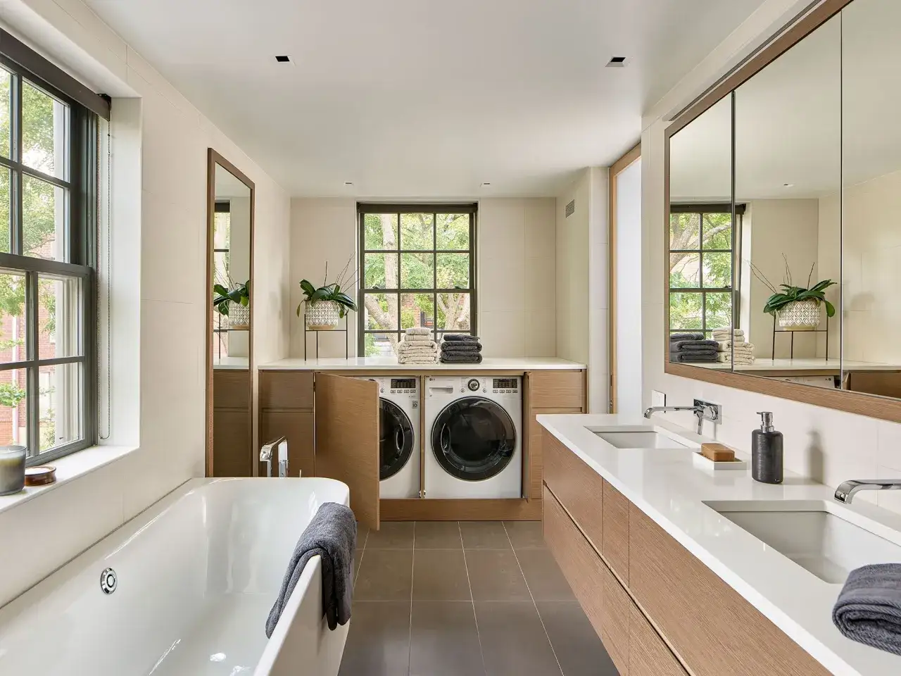 Coin buanderie dans salle de bain moderne avec baignoire, double vasque et lave-linge/sèche-linge intégrés dans des placards en bois.