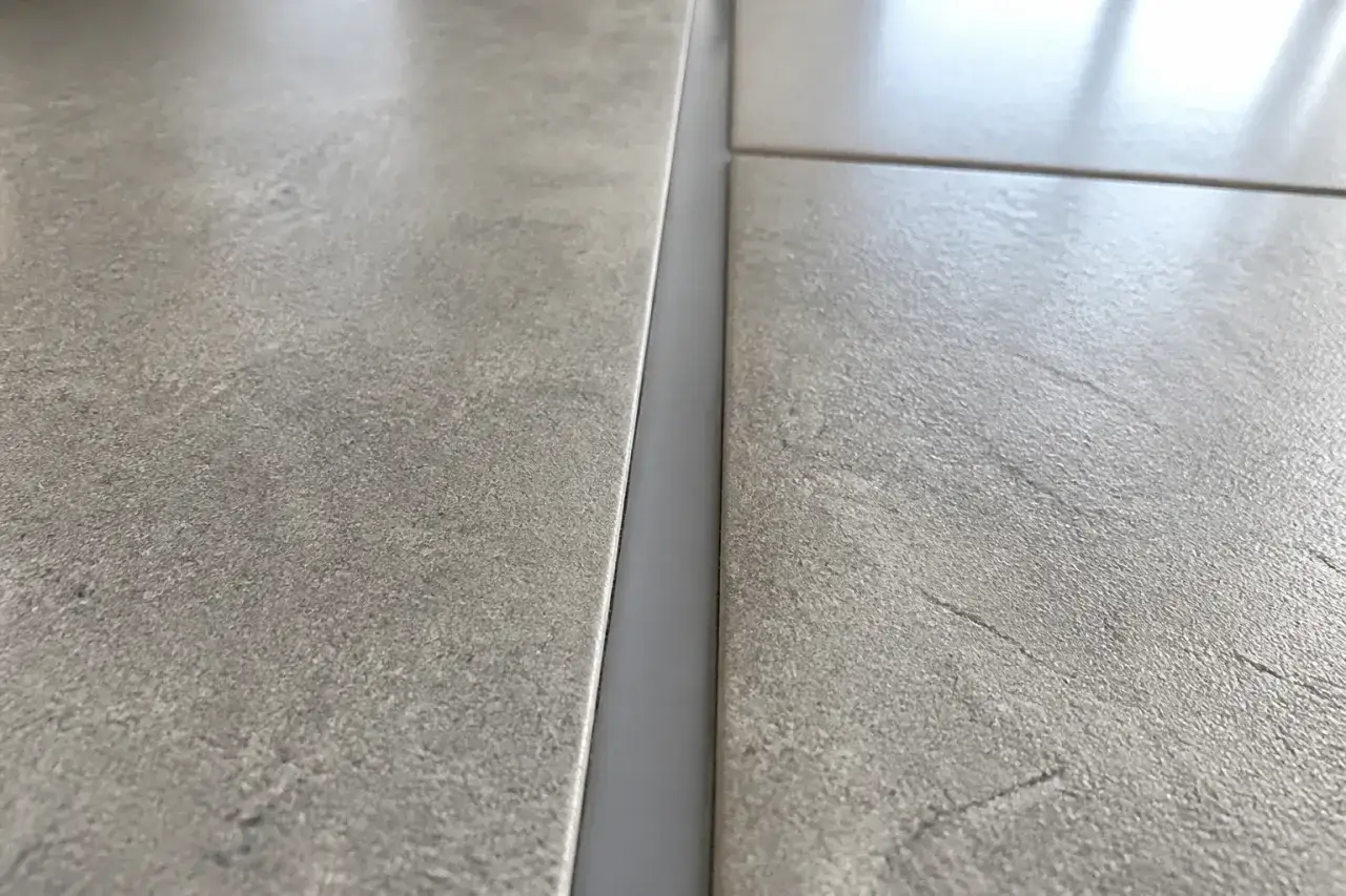 Gros plan sur un joint de dilatation carrelage gris, entre deux carreaux de sol texturés.