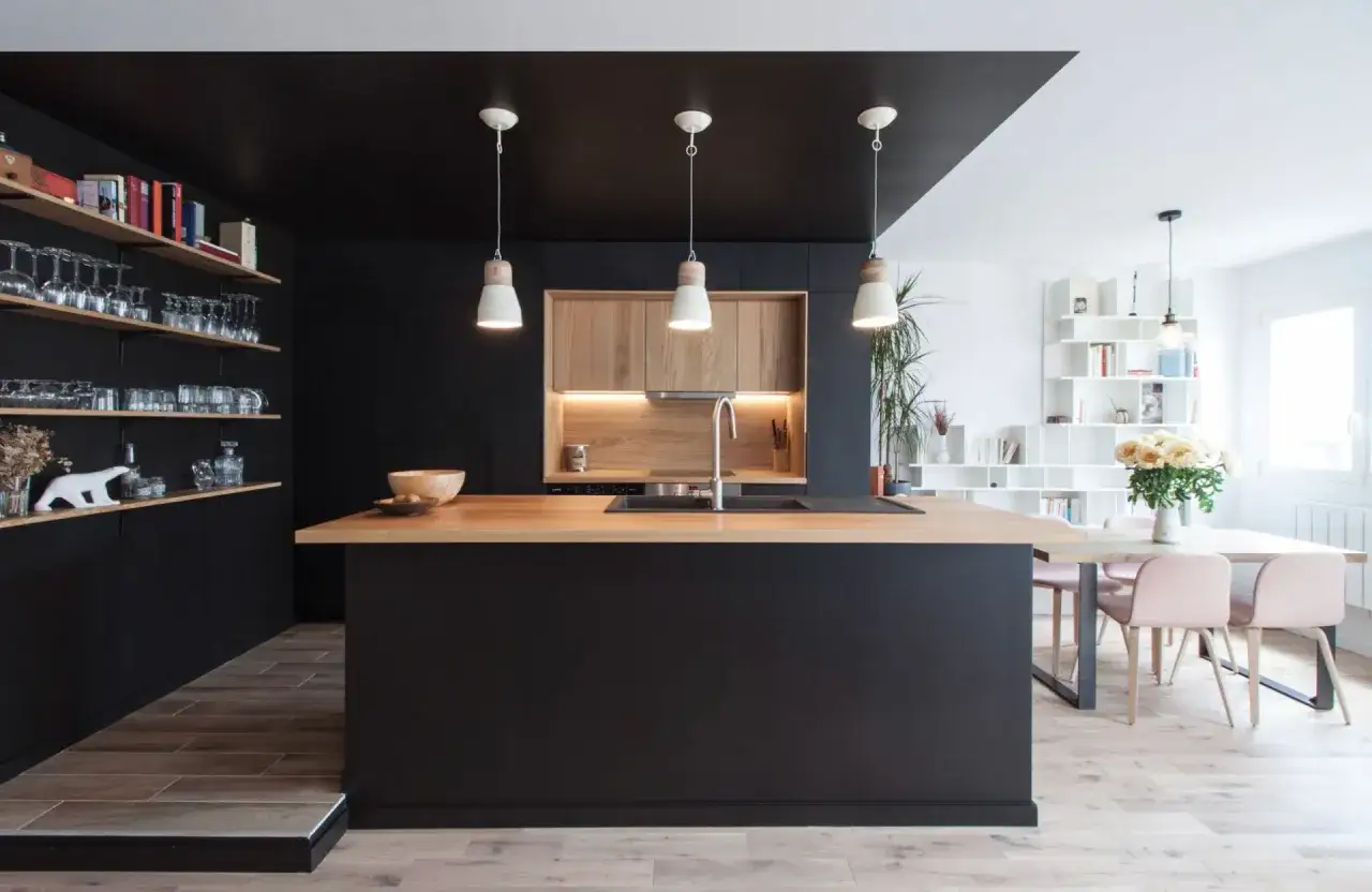 Cuisine moderne avec îlot central en bois, armoires noires et carrelage marron foncé au sol.