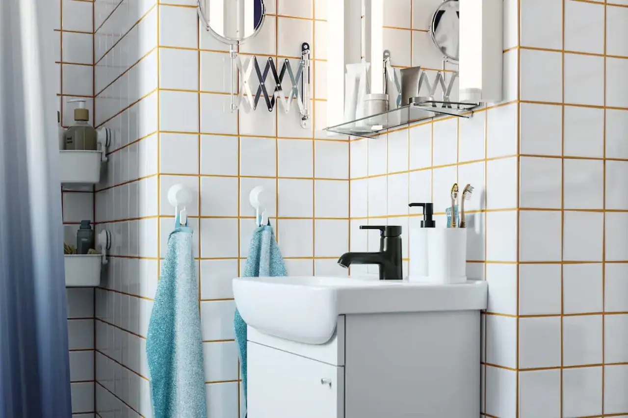 Salle de bain moderne avec carrelage blanc et joints dor&eacute;s. Un lavabo blanc, un robinet noir, des serviettes bleues et des accessoires de toilette. Quel joint pour douche ?