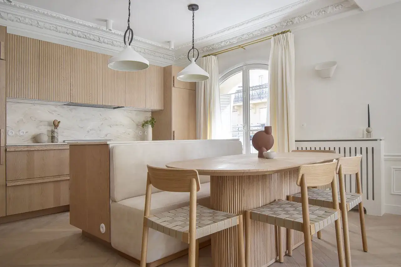 Un élégant mélange travertin et parquet habille cette cuisine-salle à manger moderne, avec des meubles en bois clair et une banquette confortable.