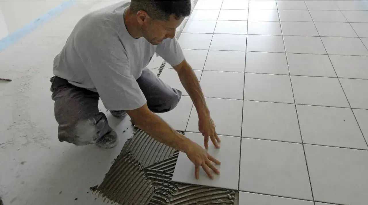 Un carreleur applique du mortier pour coller du carrelage au ciment sur un sol.