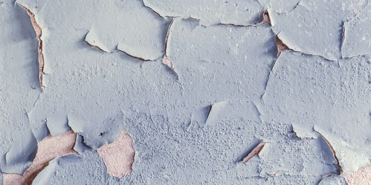 Texture d'un mur où la peinture s'écaille, révélant des couches anciennes et la matière brute.