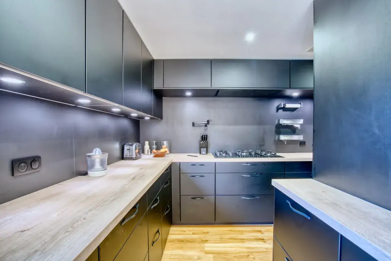 Cuisine moderne aux armoires sombres et plans de travail en bois clair. Une plaque de cuisson intégrée suggère une cuisine sans hotte visible, pour un look épuré.