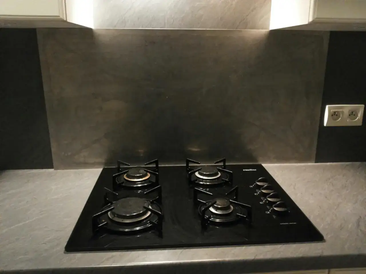 Plaque de cuisson noire &agrave; quatre feux, avec un fond en m&eacute;tal bross&eacute; sur le mur de la cuisine.