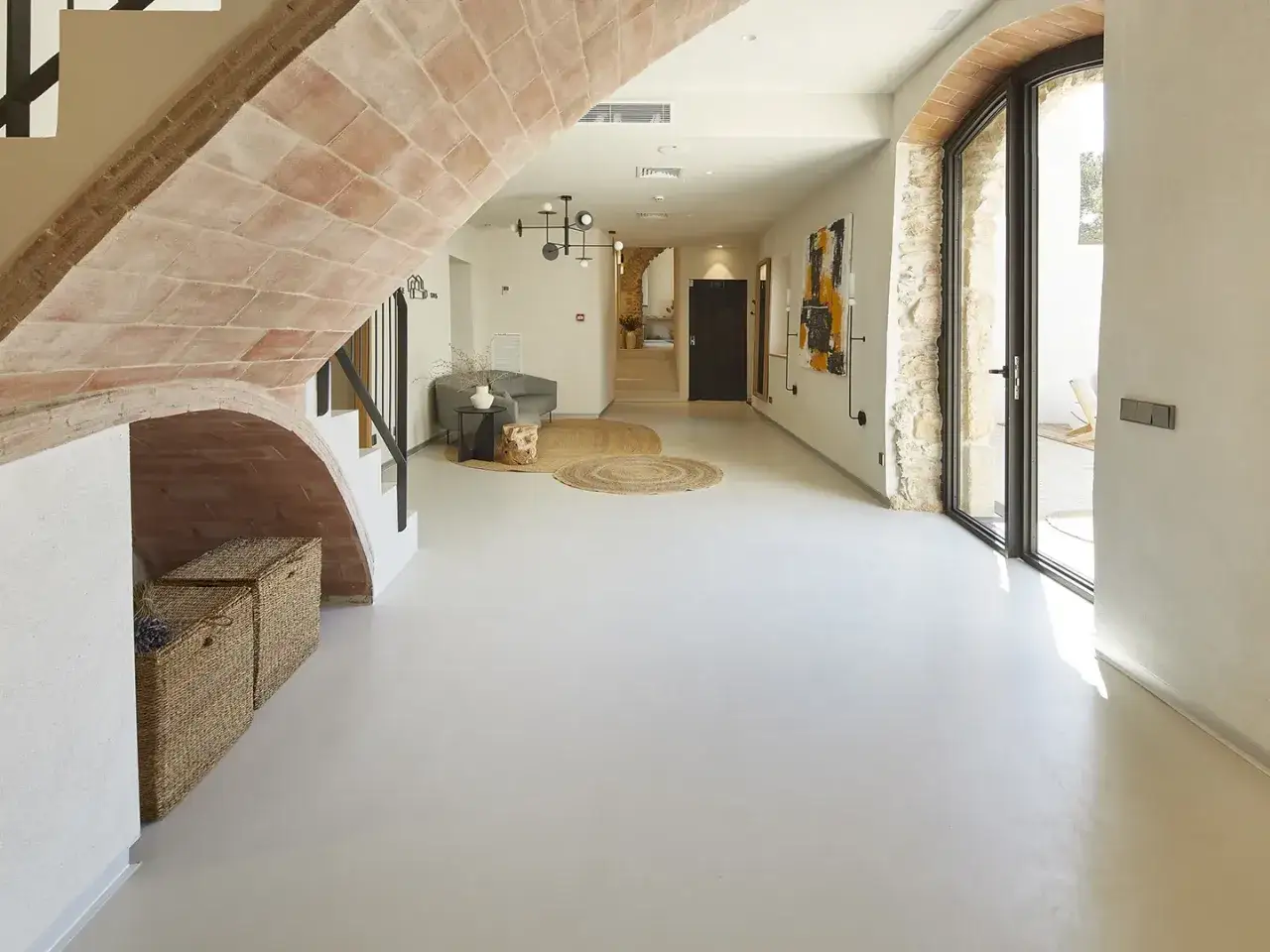 Un hall d'entrée moderne avec un sol en béton ciré sur carrelage sol, un escalier en briques apparentes et une grande baie vitrée.