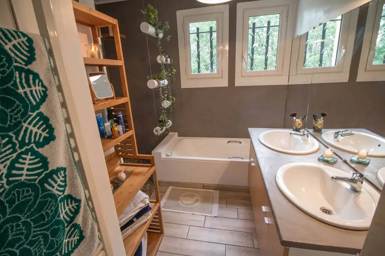 Salle de bain moderne après rénovation : baignoire, double vasque, étagères en bois, plantes suspendues. Une transformation réussie !