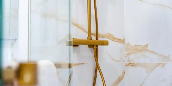 Robinet de douche doré, avec un pommeau réglable en hauteur, sur un mur carrelé de marbre blanc et or.