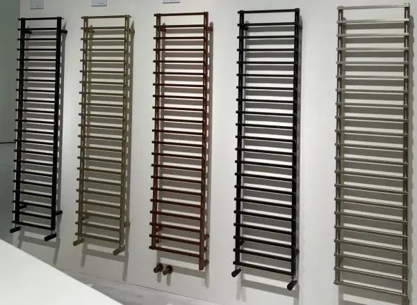 Cinq sèche-serviettes de différentes couleurs (noir, bronze, marron, noir, gris) sont alignés. La hauteur de ces sèche-serviettes est impressionnante.