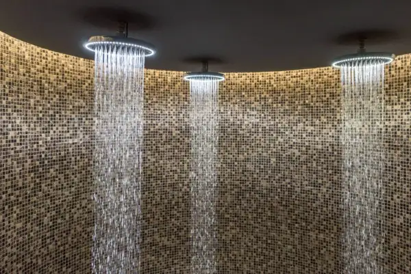 Trois douches modernes avec éclairage LED diffusent des cascades d'eau sur un mur de mosaïque. Une expérience de douche sensorielle unique.