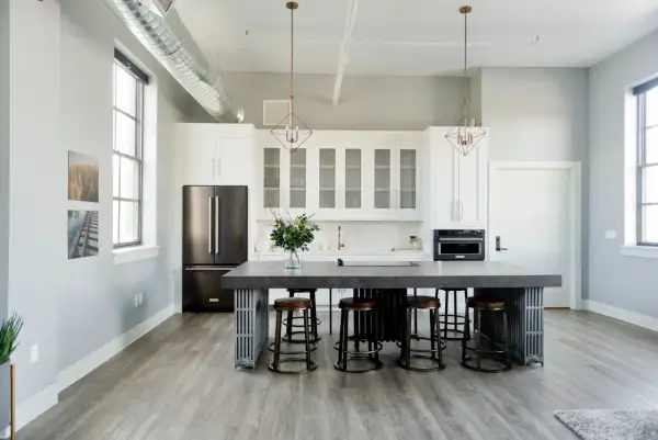 Cuisine moderne avec îlot central, tabourets et armoires blanches. Une cuisine sans hotte, avec un style épuré et industriel.
