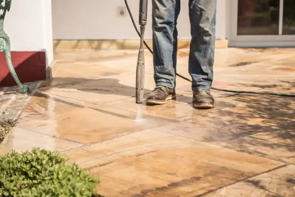 Un homme nettoie un carrelage antidérapant avec un nettoyeur haute pression. L'eau éclabousse sur les dalles.