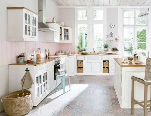 Une cuisine campagne chic lumineuse avec des meubles blancs, un plan de travail en bois, un carrelage coloré et de grandes fenêtres donnant sur le jardin.