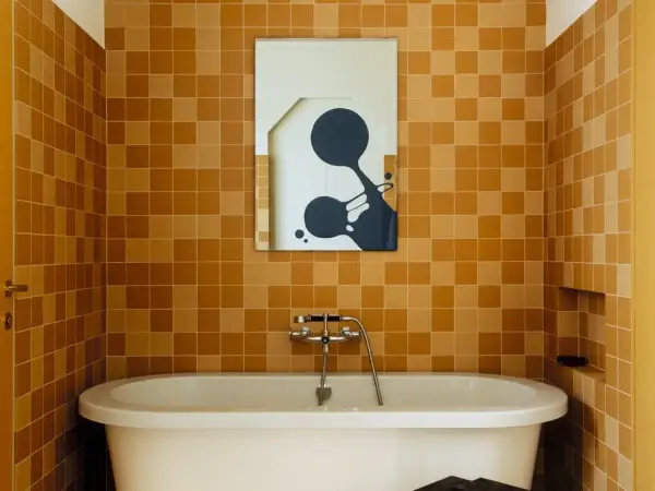 Salle de bain aux tendances carrelage ocre, baignoire blanche et miroir abstrait.