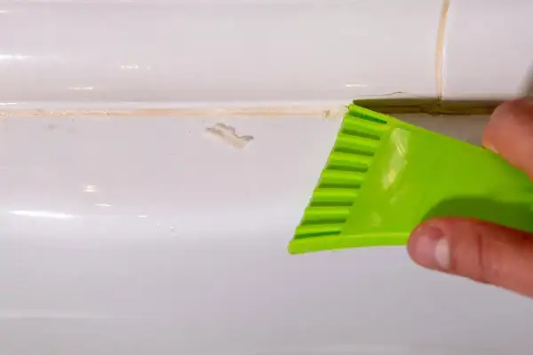 Main verte utilisée pour enlever joint silicone sale sur une surface blanche.