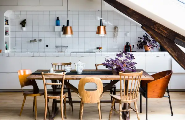Une cuisine ouverte en L avec un îlot central en bois, des chaises vintage et des suspensions cuivrées. Une plante violette apporte une touche de couleur.