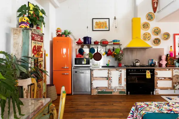 Cuisine colorée avec frigo orange vif, vaisselle suspendue et une astuce rangement cuisine : des portes de placard dépareillées pleines de charme.
