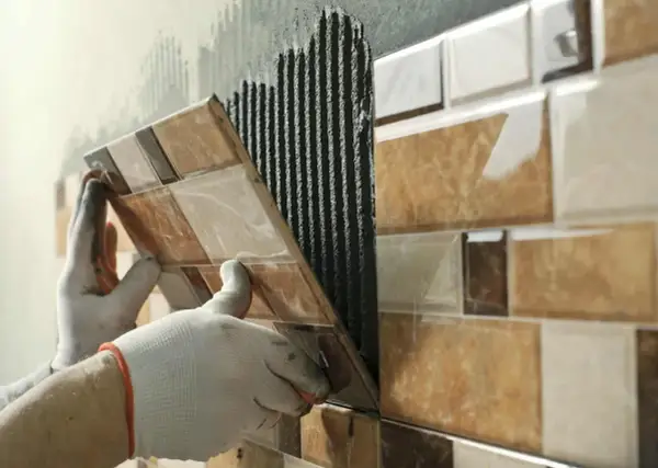 Pose de carrelage sur carrelage, une main gantée appliquant une nouvelle rangée sur le mur déjà carrelé.