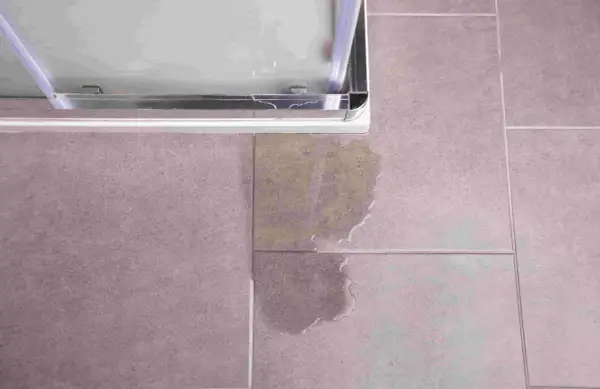 Une fuite sous le bac à douche, une situation qui peut nécessiter une intervention d'assurance. L'eau s'est répandue sur le carrelage.