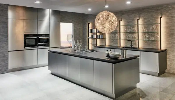 Une cuisine chic et moderne aux finitions métalliques, avec un îlot central, des fours intégrés et des étagères lumineuses.
