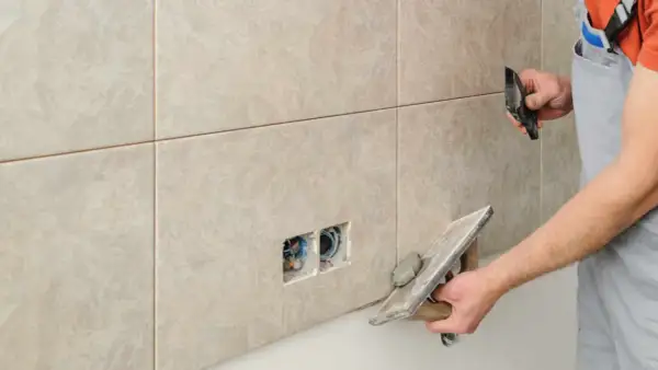 Un carreleur applique un joint époxy sur des carreaux muraux. Il utilise une taloche pour étaler le mortier.