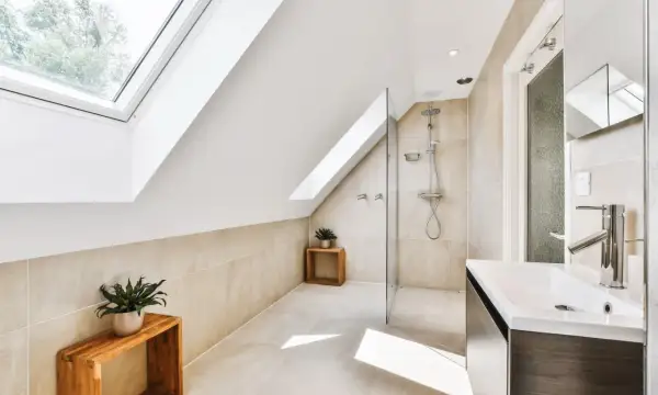 Salle de bain sous pente avec douche à faible hauteur, lavabo moderne et puits de lumière.