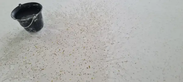 Un seau d'eau éclabousse un sol en terrazzo blanc moucheté, révélant comment faire briller un sol en terrazzo.