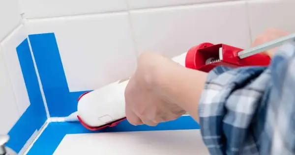 Application d'un joint silicone blanc avec un pistolet pour assurer l'étanchéité de la douche. Le bon quel joint pour douche est essentiel.