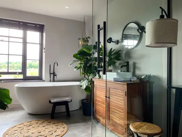 Une baignoire îlot, un meuble en bois et une plante luxuriante créent une ambiance de wet room apaisante.