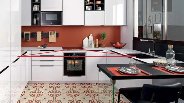 Cuisine moderne avec une organisation optimisée : tiroirs blancs, four encastré, crédence orange, et un îlot noir pour les repas.