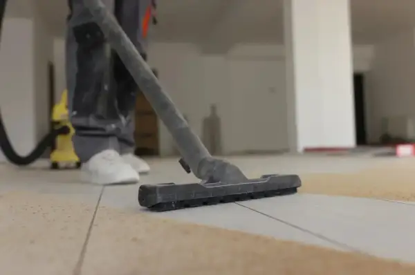 Un ouvrier utilise un aspirateur pour nettoyer le carrelage après le jointoiement. La poussière et les débris sont aspirés.