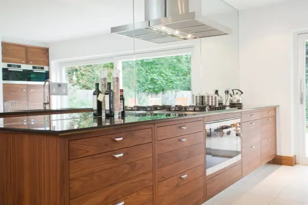 Cuisine moderne avec îlot central en bois, hotte en inox et vue sur jardin. Une belle rénovation pour une vieille cuisine.